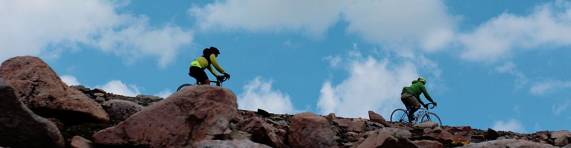 Zwei Radfahrer von Single Aktiv Reisen fahren auf einem felsigen Hang mit Blick auf eine bergige Landschaft